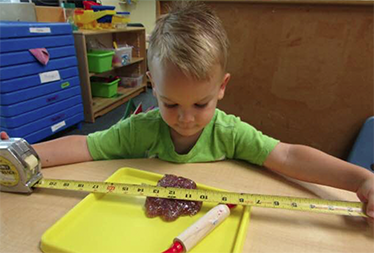 Little boy measuring dough with a tape measure